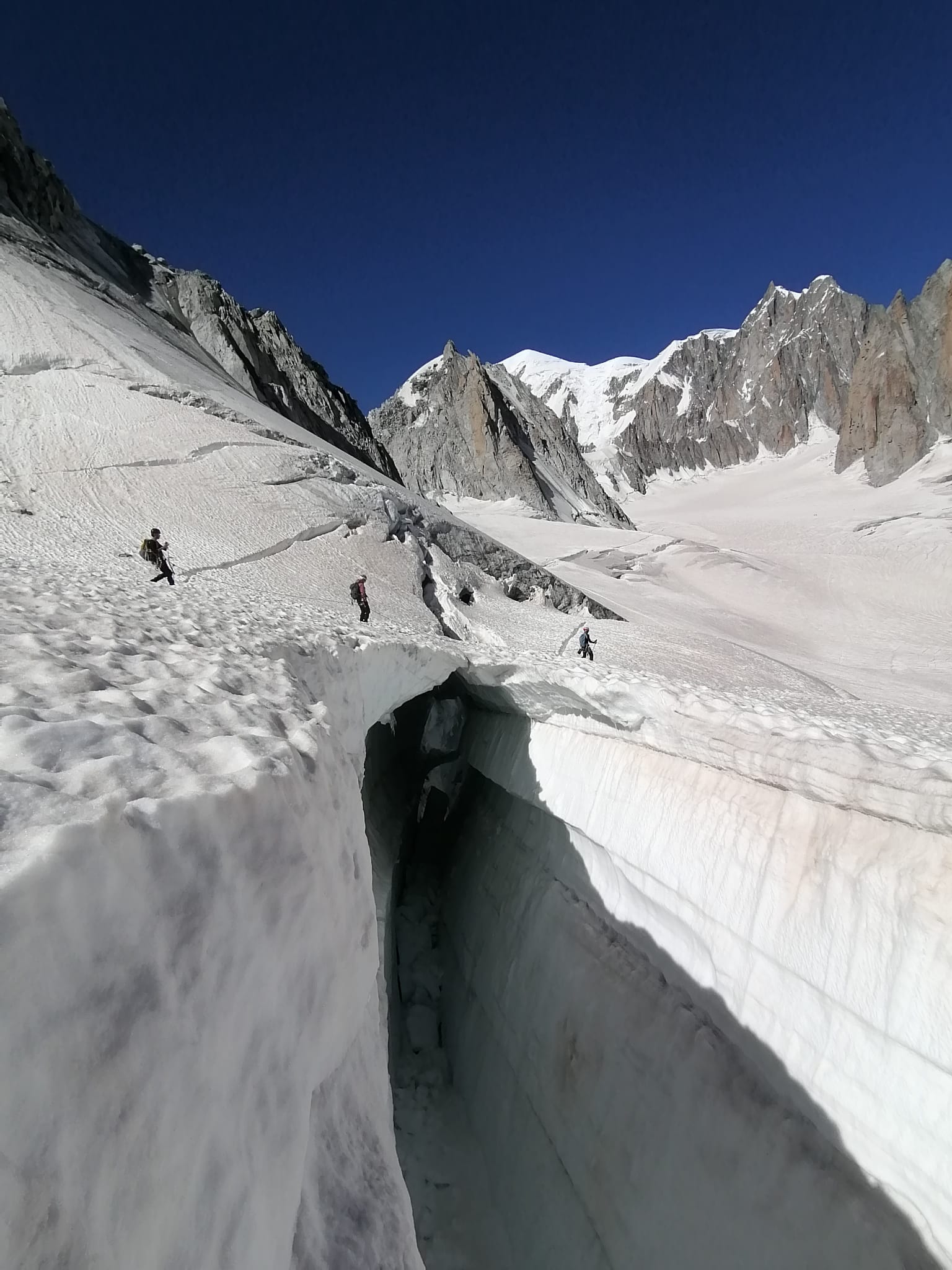 Three climbers cross a precarious snow bridge on the Vallée Blanche
